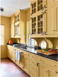 a large kitchen with yellow cabinets and black counter tops, along with a basket of vegetables on the island