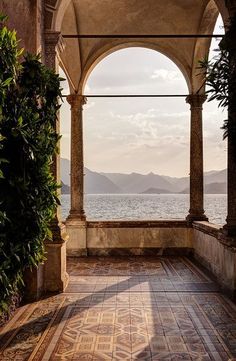 an archway leading to the ocean with mountains in the distance and tiled flooring on either side