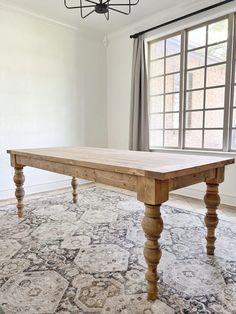 a large wooden table sitting on top of a rug in a living room next to a window