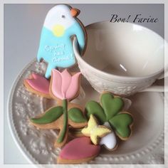 some decorated cookies are on a plate next to a cup and saucer with a bird