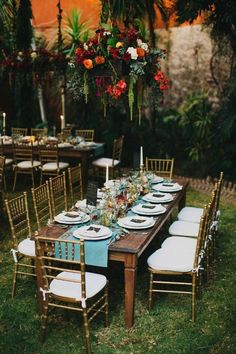 an outdoor dinner table set up with white and blue linens, gold chairs, and flowers