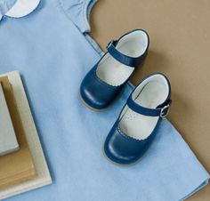 a pair of baby shoes sitting on top of a blue blanket next to a book