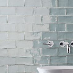 a white sink sitting under a faucet next to a green tiled wall