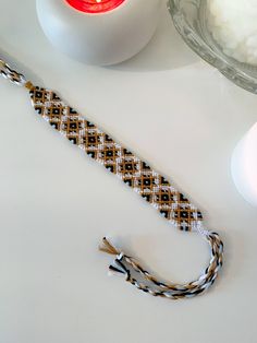 a braided bracelet sitting on top of a white table next to a red candle