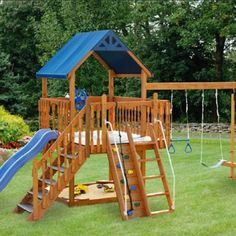 a wooden swing set with a blue roof and slide in the grass next to trees