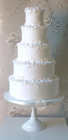 a white wedding cake sitting on top of a table next to a floral wallpaper