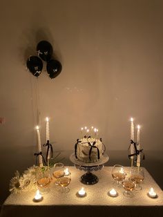 a table topped with a cake covered in white frosting and lit candles next to black balloons