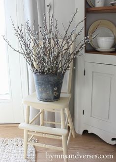 a white chair sitting in front of a window next to a vase filled with flowers