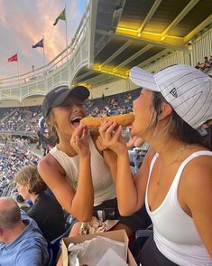 two women eating hot dogs at a sporting event