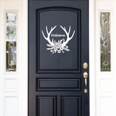 a black front door with white deer antlers and welcome stickers on the side