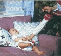 a woman holding a baby on top of a purple couch next to another person in a white dress