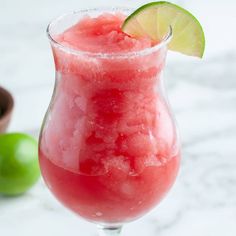 a watermelon drink in a glass next to limes