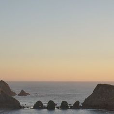 an airplane flying over the ocean with rocks in the foreground and water on the far side