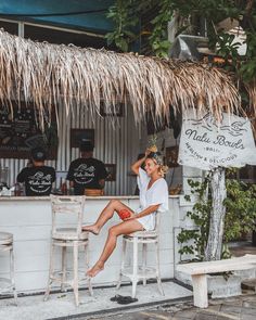 a woman sitting at a bar in front of a tiki hut with thatched roof