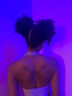 a woman with a tattoo on her back standing in front of a purple wall and wearing a white tank top