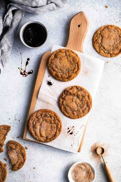 chocolate chip cookies on a cutting board with spoons next to it and two cups of coffee in the background