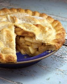 an apple pie in a blue bowl with one slice missing from it's crust