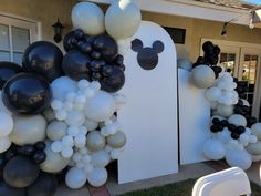 mickey mouse balloons are on display in front of a house that is decorated with black and white balloons