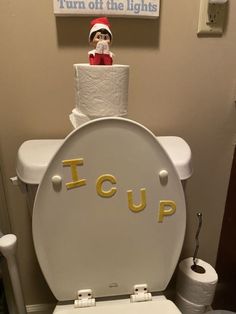 a toilet with a sign on the lid that says icup and a santa hat