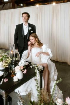 a man and woman sitting at a table with flowers in front of them on their wedding day