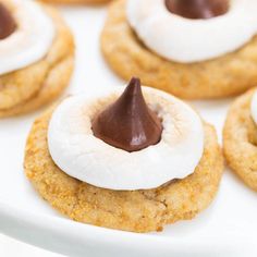 small cookies with marshmallows and chocolate on top are arranged on a white plate