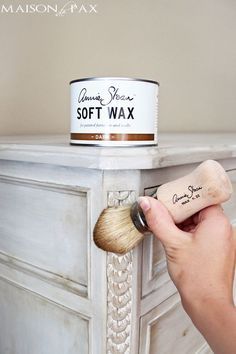 someone using a brush to paint a white dresser with soft wax on it's top