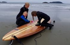 two women and a child are on the beach with a surfboard in front of them