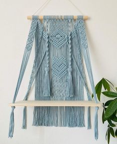 a blue wall hanging with tassels and wooden pegs next to a potted plant