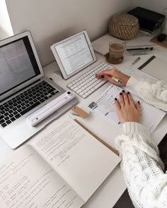 a person sitting at a desk with two laptops and papers on the table next to them