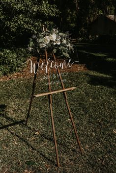 a welcome sign in the grass with flowers on it and greenery behind it that says welcome