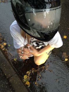 a woman wearing a helmet sitting on the ground next to a puddle with her hands under her face