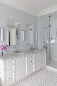 a white bathroom with two sinks, mirrors and a shower stall in the corner is shown