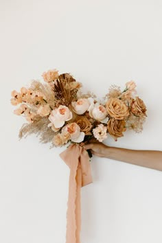 a person's hand holding a bouquet of flowers on a white wall with brown ribbon