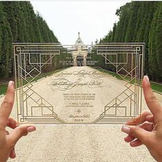 two hands holding up a card in front of an entrance to a building with trees on both sides