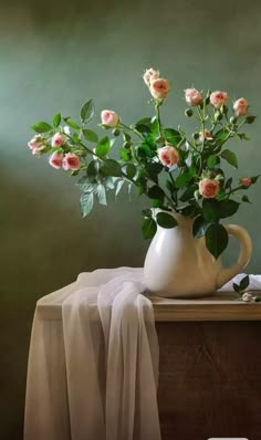 a white vase filled with pink roses on top of a wooden table next to a green wall