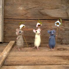 three little mice sitting on top of a wooden floor next to each other with flowers in their ears