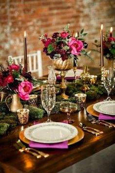 the table is set with gold and pink plates, silverware, and flowers in vases