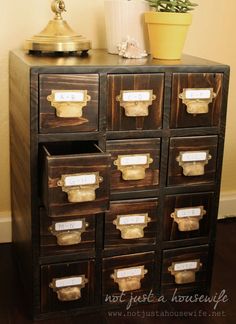 an old wooden cabinet with many drawers and labels on the doors, next to a potted plant