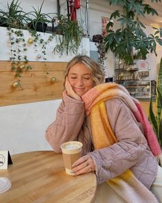 a woman sitting at a table with a cup of coffee in front of her face