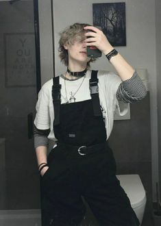 a young man taking a selfie in the bathroom while wearing overalls and suspenders