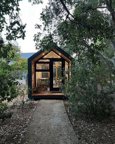 a tiny cabin nestled in the woods on a dirt path leading to a tree filled area