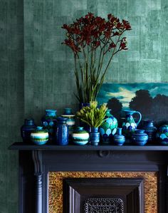 a mantle with vases and flowers on it in front of a striped wallpaper