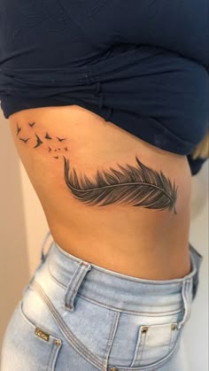 a woman's stomach with a feather and birds tattoo on her side ribcage