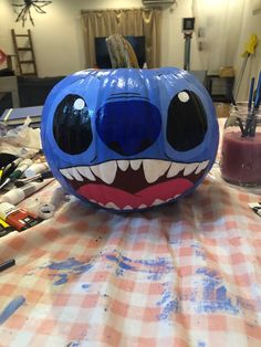 a blue pumpkin with an evil face painted on it sitting on a checkered table cloth