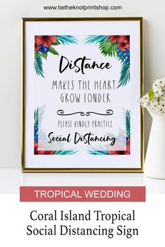 a tropical wedding sign with flowers and greenery in the frame on a white table