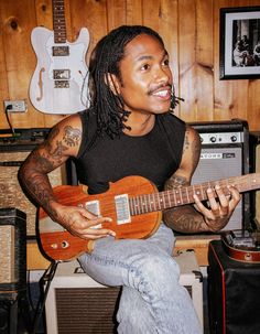 a man with dreadlocks playing an electric guitar in a room full of guitars