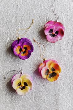 three different colored pansies hanging from hooks on a white surface, one is purple and the other is yellow