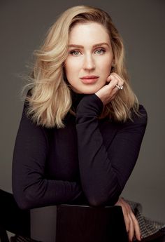 a woman sitting on top of a chair with her hand under her chin and looking at the camera