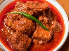 a bowl filled with meat and red sauce on top of a wooden table next to a green pepper