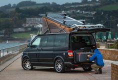 a man fixing the roof on a van with solar panels and water in the background